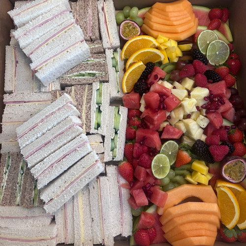 Box containing assorted sandwiches and a fruit platter.